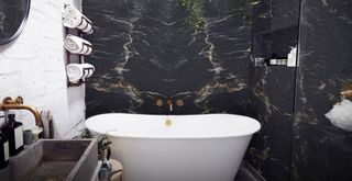 spa-like bathroom with dark marble walls and a white freestanding bath with a towel rail above the bath with rolled towels like a spa to demonstrate bathroom trends 2023