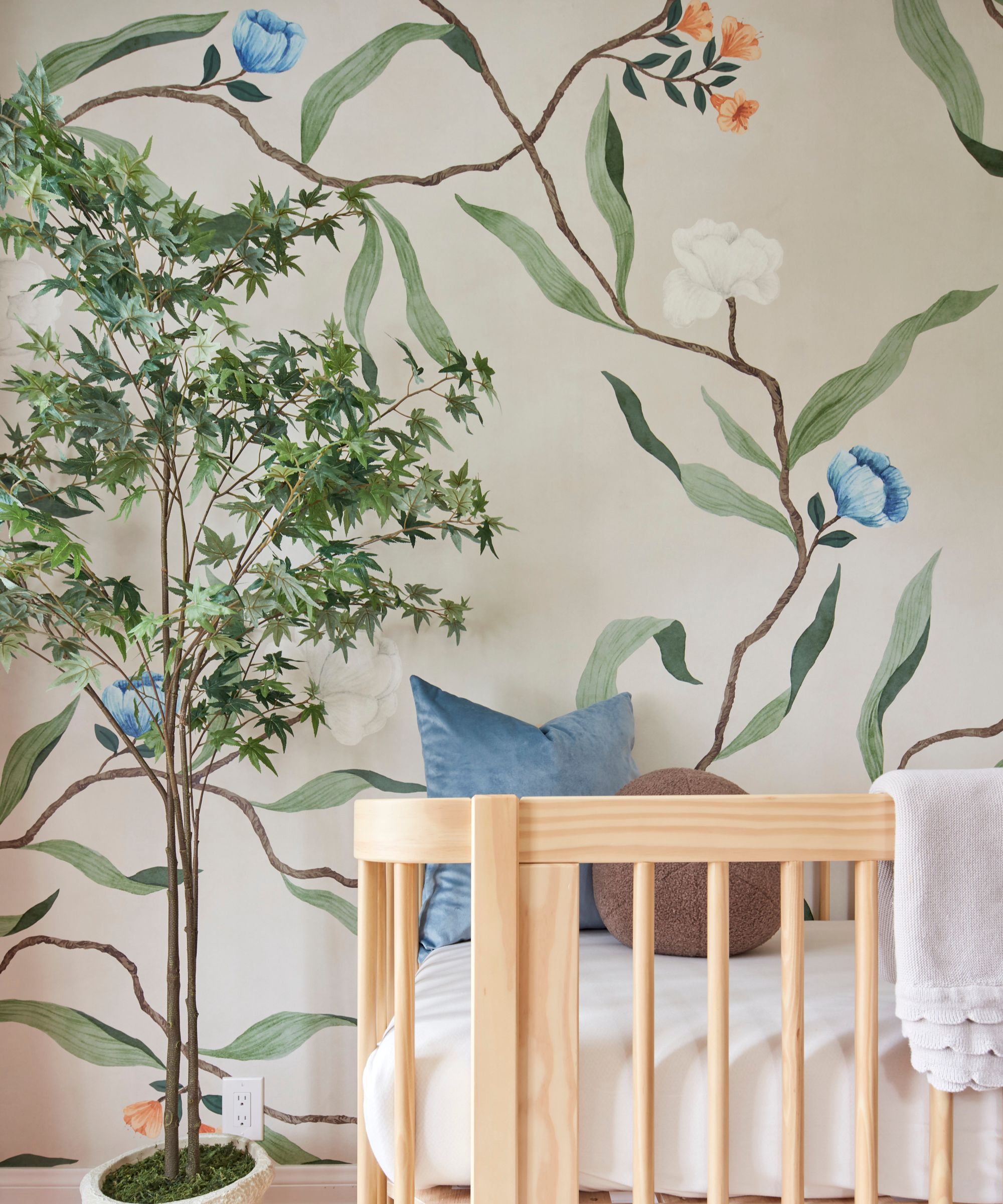 baby nursery with large wallpaper mural with pastel florals and a light oak cot