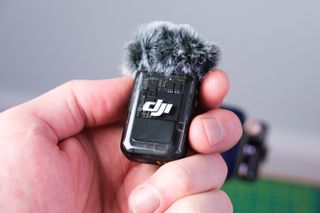 A photo of the DJI Mic 2 (TX unit) in hand with a wind shield fitted.