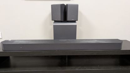 Samsung HW-Q990H soundbar system with the soundbar in front, subwoofer behind and rear speakers stacked on subwoofer 
