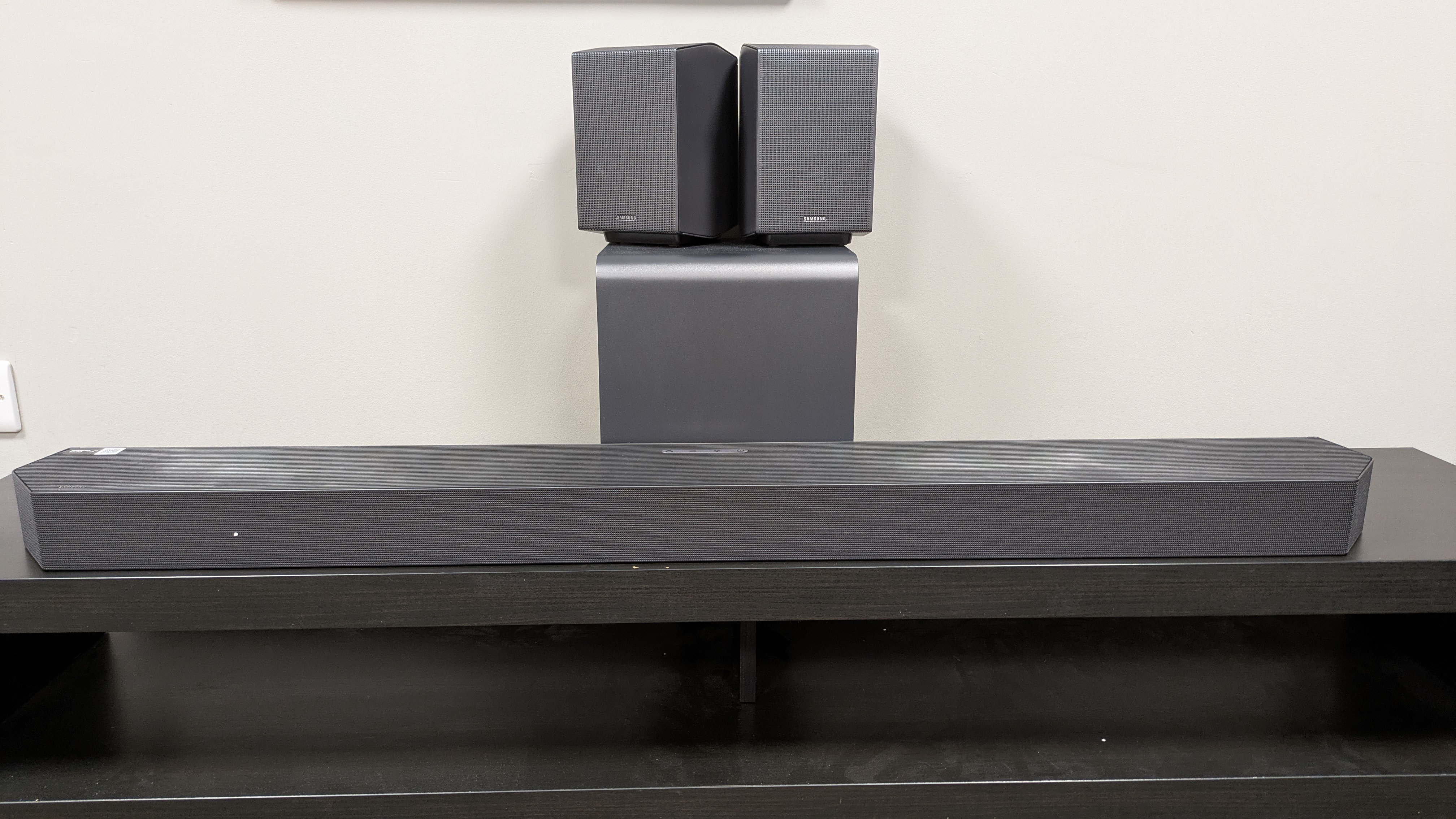 Samsung HW-Q990H soundbar system with the soundbar in front, subwoofer behind and rear speakers stacked on subwoofer 