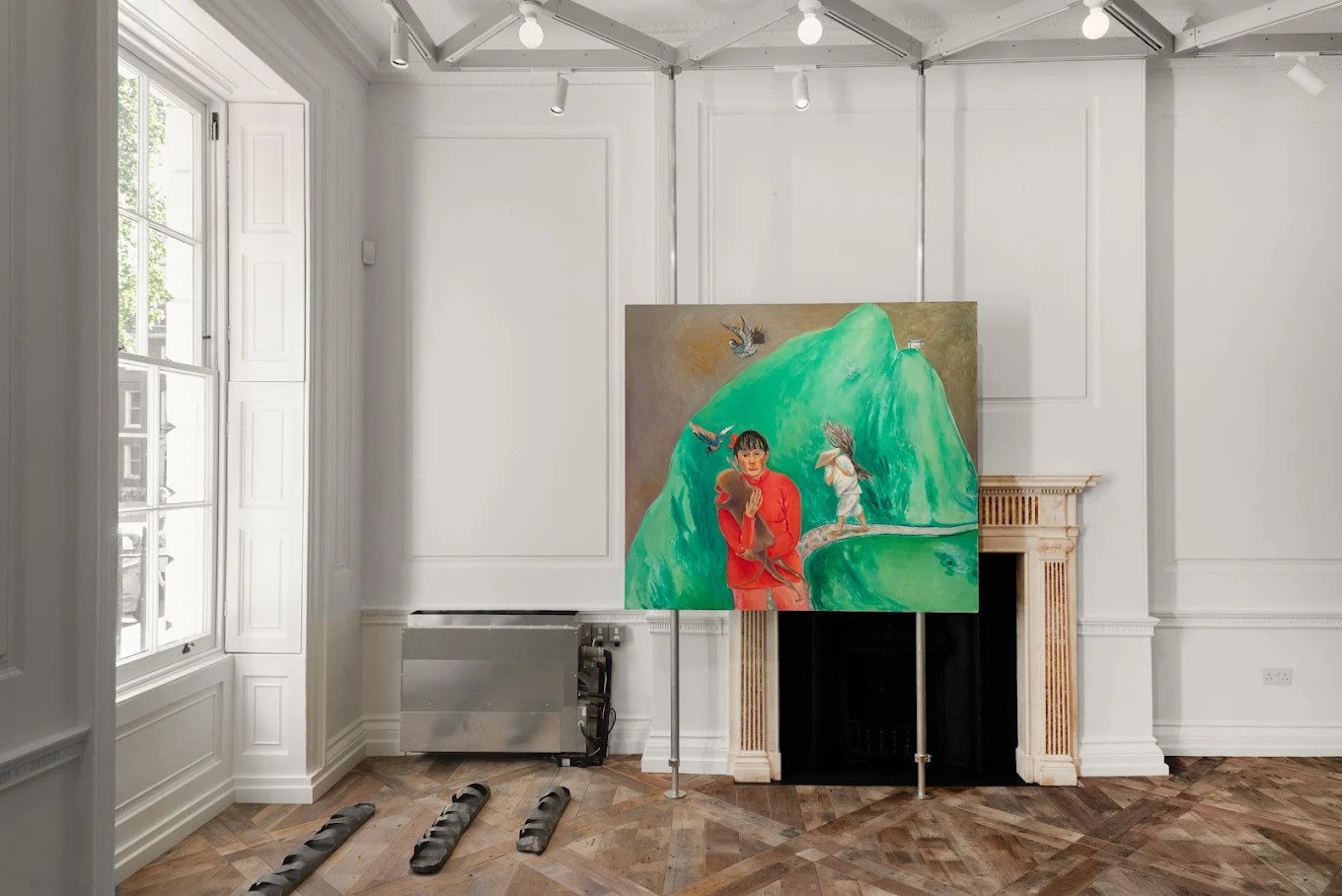 A naturally lit art gallery with wooden floors and a fantastical mountain scene captured in a painting, with a couple of human silhouettes set against a green peak.