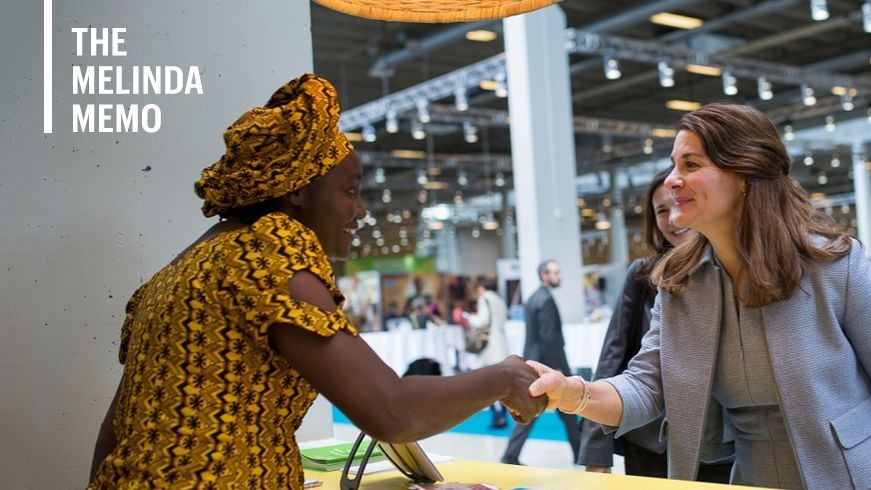 Two women shake hands across a trade show booth counter.