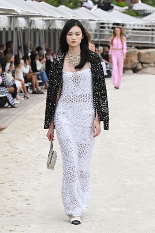 A model walks the Chanel runway wearing a white crochet gown.