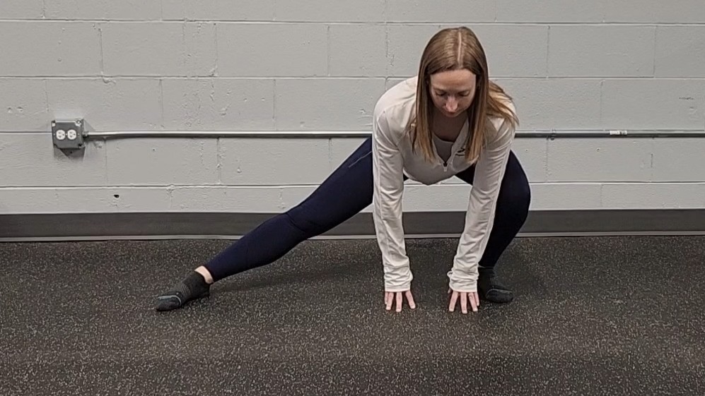 Woman demonstrating stretch. She wears a white long-sleeve top, blue sports leggings and black socks
