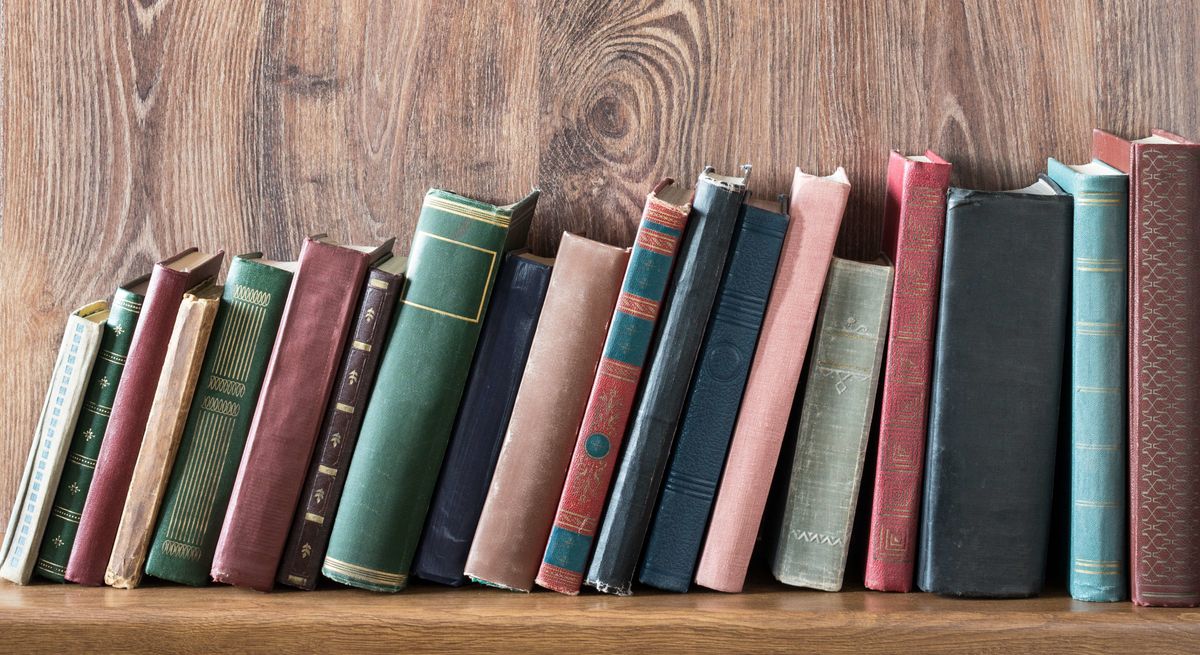 Old books leaning over on a wooden bookshelf