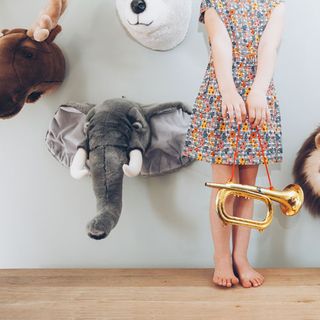 A girls in a dress holding a trumpet in front of a wall of toy animal heads
