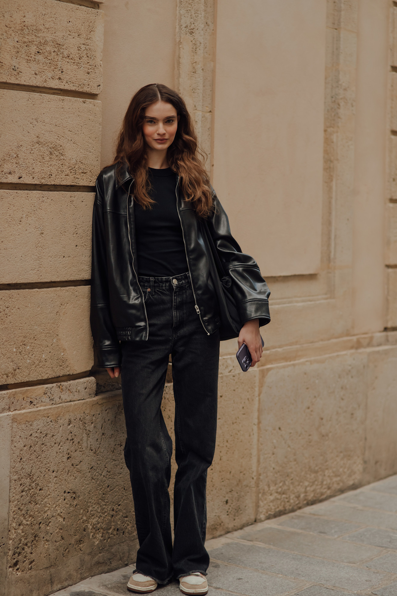 woman wearing leather jacket, black top, jeans, and sneakers