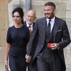 Victoria Beckham walks hand-in-hand with David Beckham, wearing a navy dress with black croc-print heels and a black croc bag.