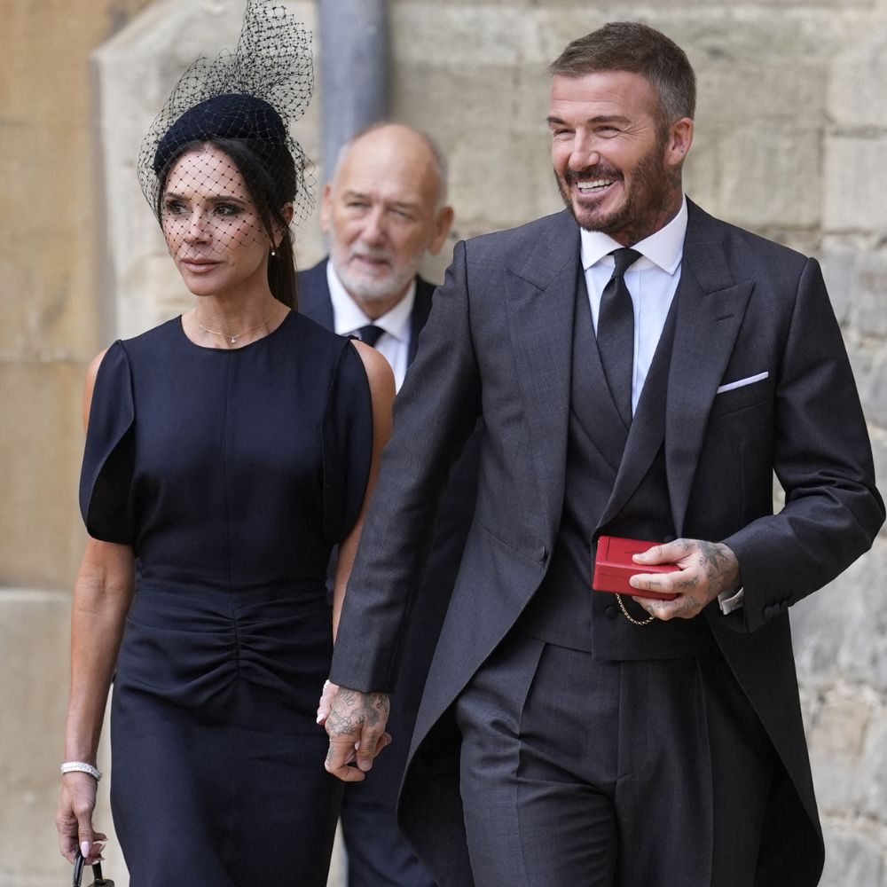 Victoria Beckham walks hand-in-hand with David Beckham, wearing a navy dress with black croc-print heels and a black croc bag.