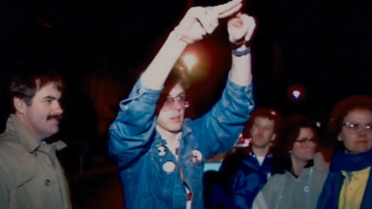 ジェリー・コーヴェルは、ドキュメンタリー番組『Deaf President Now!』で群衆に座るようサインする。