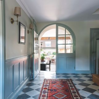 Large hallway with chequerboard marble flooring, colourful runner and blue-green walls and doors