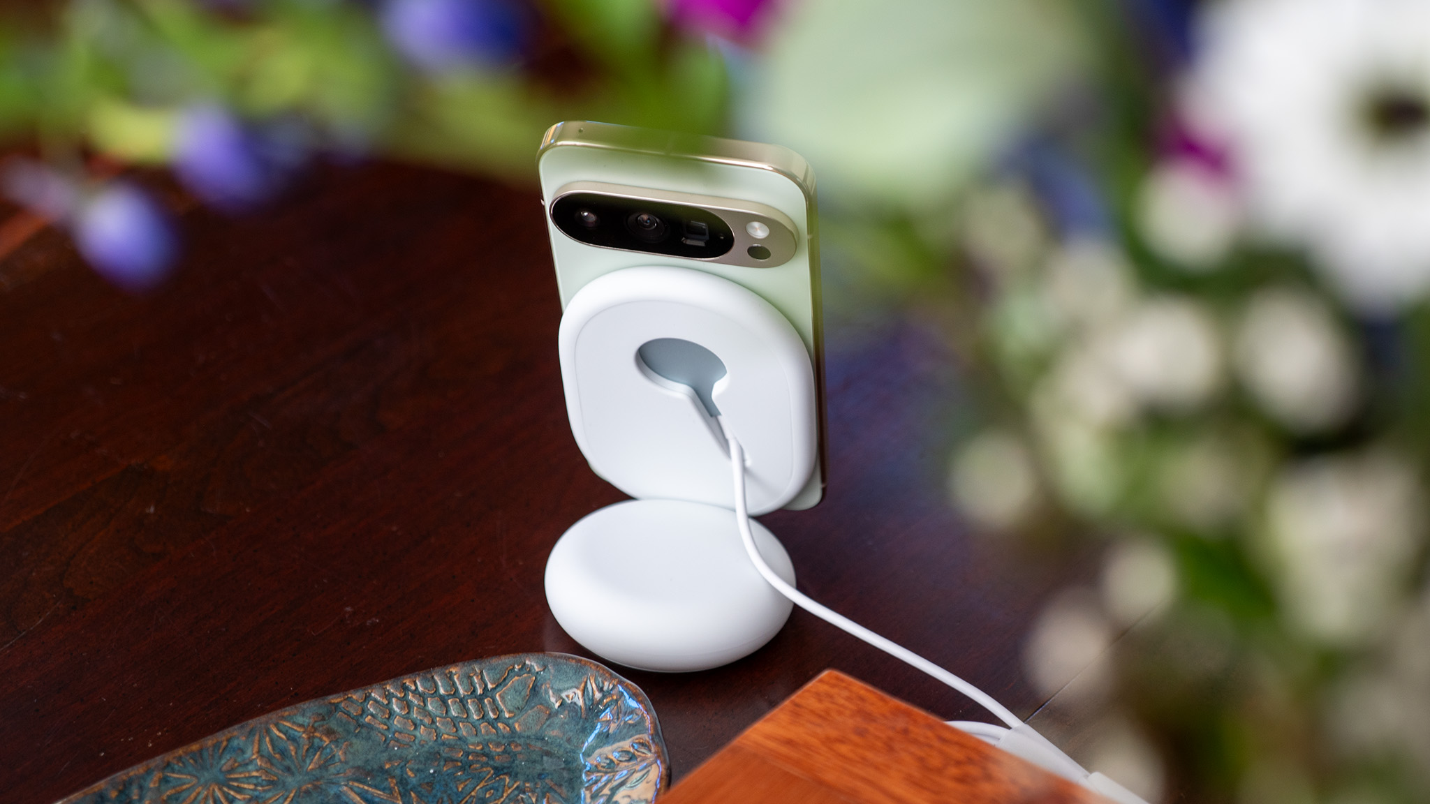 A jade Google Pixel 10 Pro on a Pixelsnap magnetic wireless charger under a ring of flowers