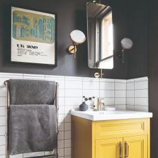 A black-painted bathroom with a yellow under-sink cabinet and grey towels hanging on a radiator