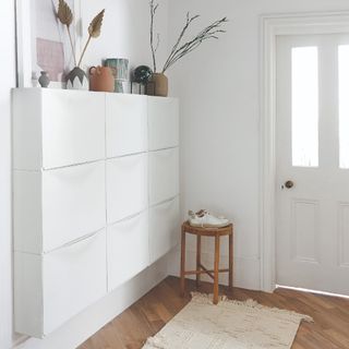 A white hallway with nine IKEA shoe cabinets mounted to the wall and displaying decor on top