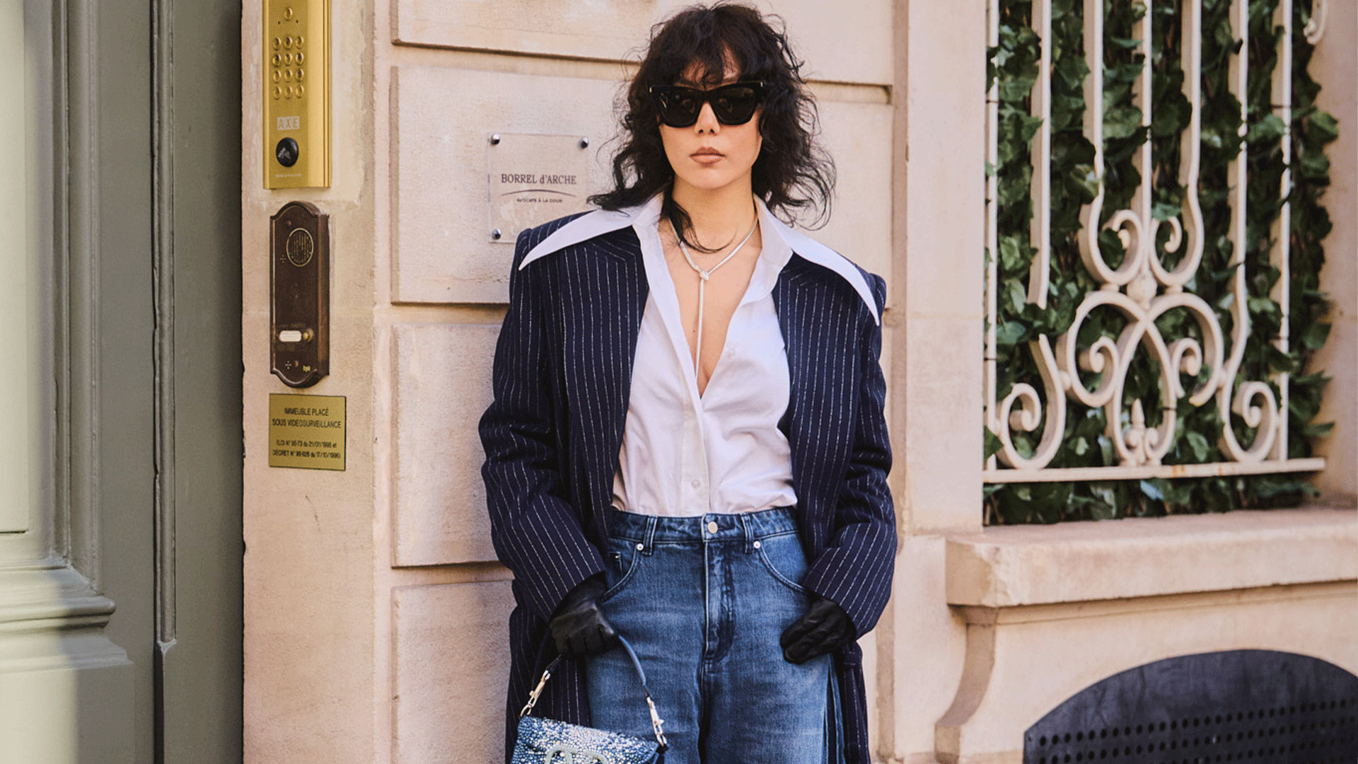 woman wears white button down, pinstripe duster coat, wide-leg jeans, and a mini denim valentino bag