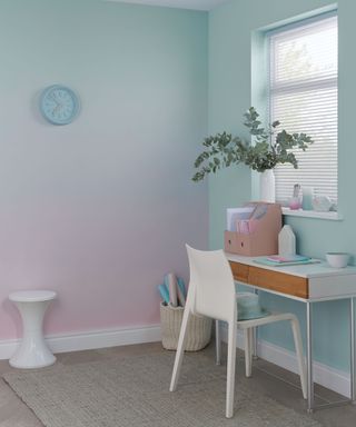 Pink and green ombre wall decor in home office, with small white desk and chair, and a storage basket in the corner and small white side table