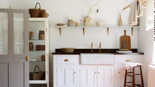 A light-filled utility room with a marble sink, brass taps, shaker cabinetry, rustic ceramics, and natural wood accents in a soft, vintage palette