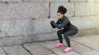 Woman runner performing squat exercise outdoors