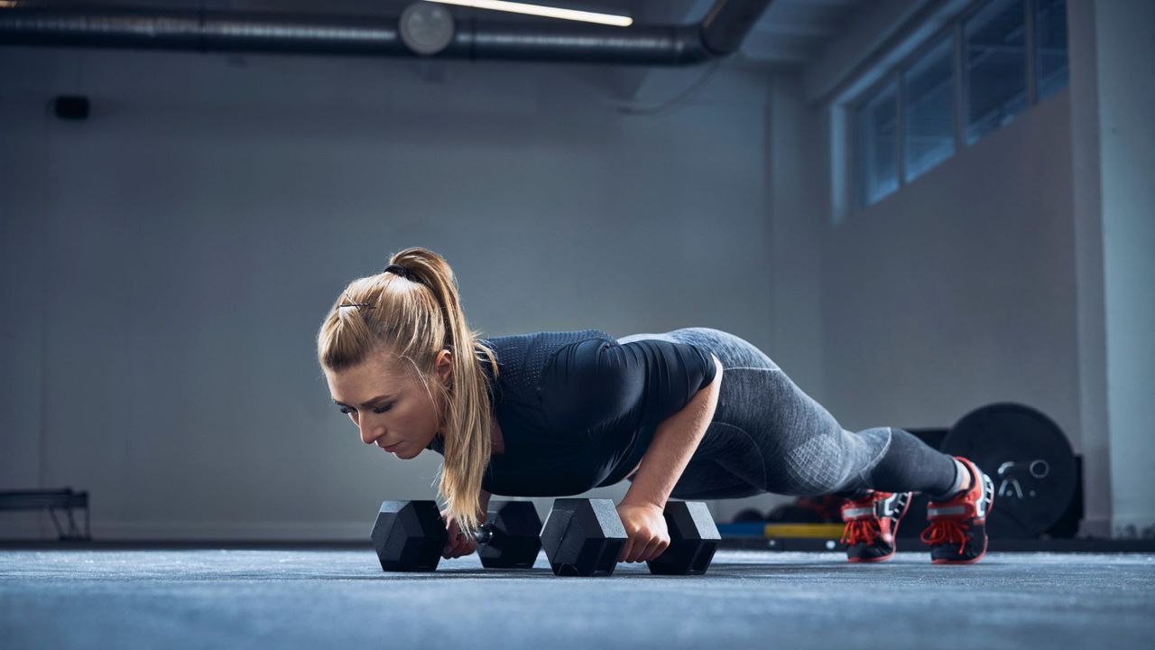 A woman performing a push-up on a pair of dumbbells at the gym