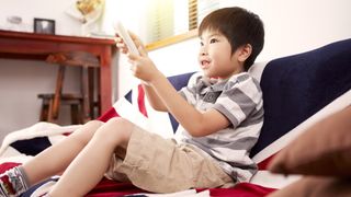 Child watching TV with remote, sitting on Union Jack blanket