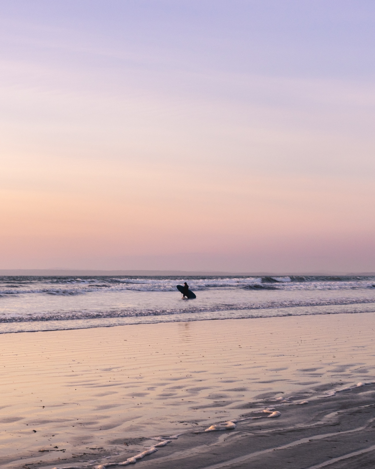 صورة لراكب أمواج وحيد بعيد يقف في أمواج لطيفة على الشاطئ.