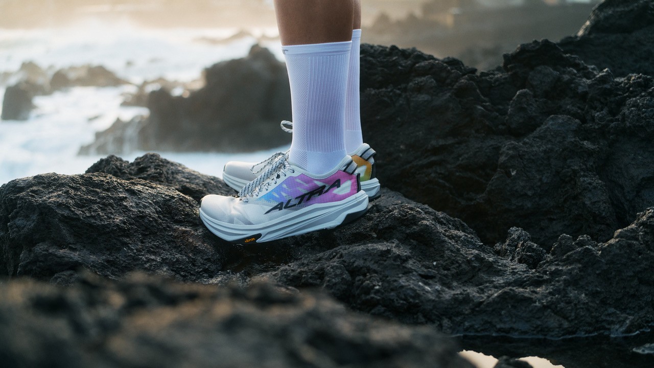 A runner&#039;s feet wearing the Altra X SOAR Mont Blanc Carbon Trail Shoes staning on rocks by the sea