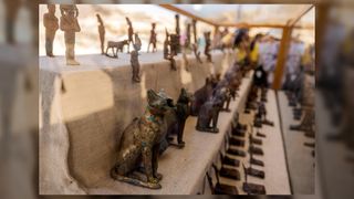 Statuettes and figurines depicting cats and Egyptian deities found in a cache dating to the Egyptian Late Period (around the fifth century BC). There are many bronze statues depicting various Egyptian gods and goddesses, such as Bastet, Anubis, Osiris, Amunmeen, Isis, Nefertum, and Hathor.