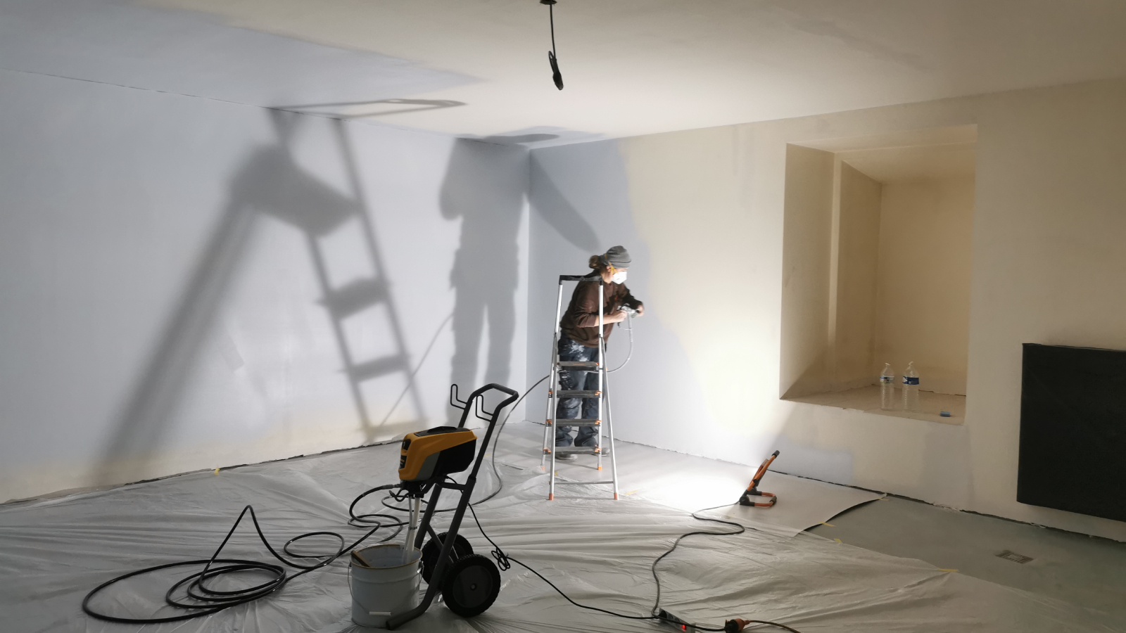 female spray painting walls of room with no windows