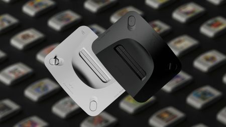 Analogue 3D consoles in white and black with blurred games on black surface in backdrop.