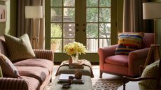A cozy living area with green walls, a striped sofa, a pink armchair, and large glass doors opening to a patio