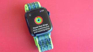 Close-up of the Apple Watch SE 2022 on a red background and Apple's Activity app where you can now pause Rings