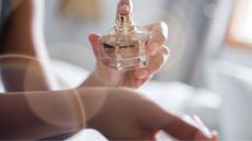 A woman's hand spraying a pink and gold perfume bottle onto her wrist