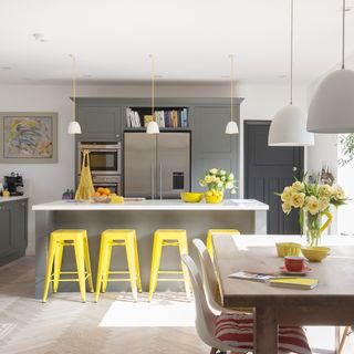 A grey kitchen with a central island and bridge yellow bar stools