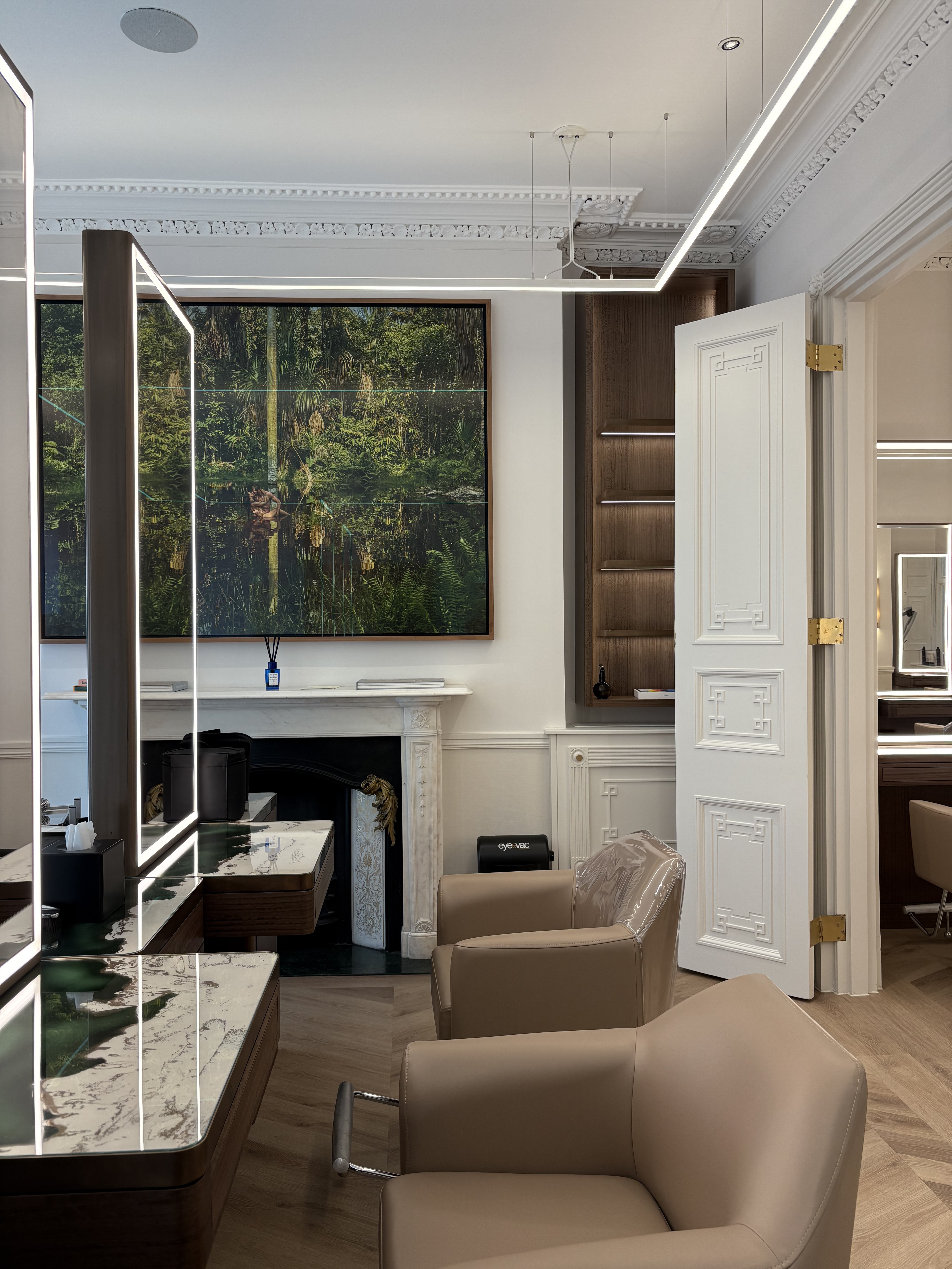A strikingly lit beauty salon sited within a historical, thoroughly renovated townhouse revives its architectural volumes through contemporary lighting, plush leathery furnishings, and sleek countertops.