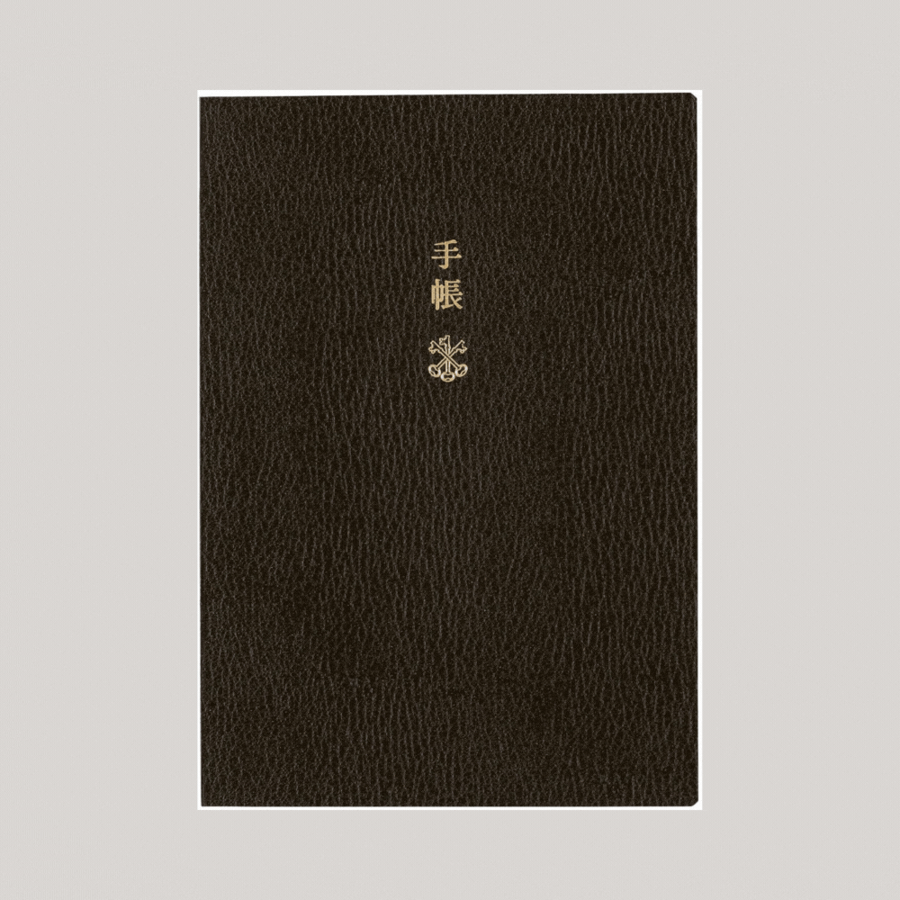 A leather notebook with a dark brown cover and Japanese characters in carved gold is shown in a revolving gift alternating with its checkered interior.