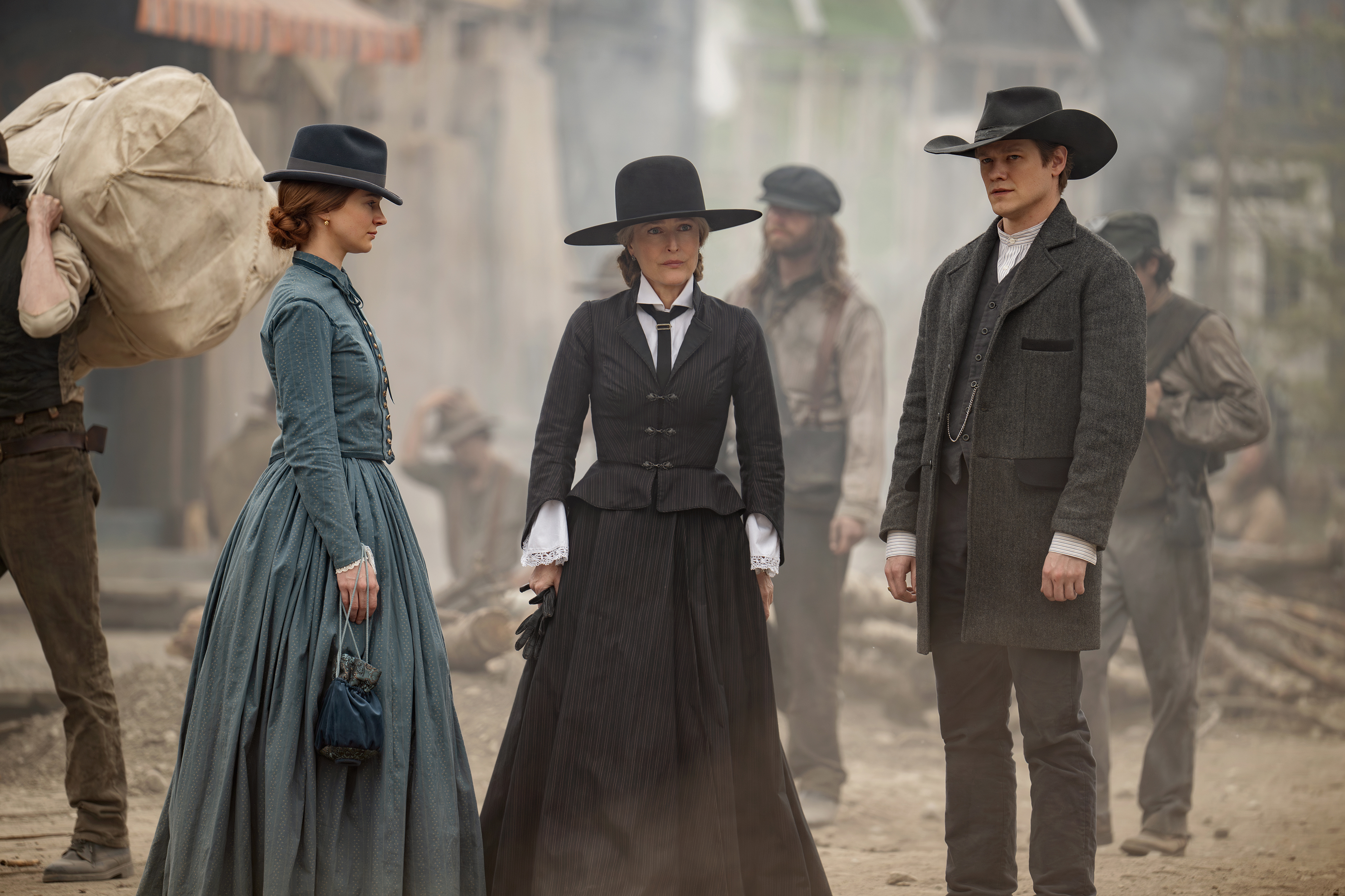 Aisling Franciosi as Trisha Van Ness, Gillian Anderson as Constance Van Ness and Lucas Till as Garret Van Ness in the abandons wearing long dresses or a suit and cowboy hands in the center of a ranch town in the abandons