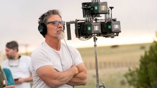 Josh Brolin directing episode 6 of Outer Range season 2, looking at something with glasses and headphones on next to a camera.