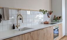 Kitchen with white countertops and wall tiles, wooden cupboards and house plants for color