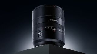 A sleek 24mm F1.8 camera lens is displayed on a dark surface, highlighting its detailed focus ring and modern design