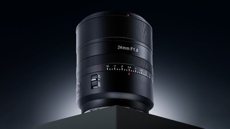 A sleek 24mm F1.8 camera lens is displayed on a dark surface, highlighting its detailed focus ring and modern design