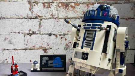 Lego R2-D2 with tools out beside an R2 minifig on display plaque and Darth Malak, all against a brick wall