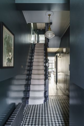 A moody blue entryway with check tiled floor and a neutral runnner up visible stairs.