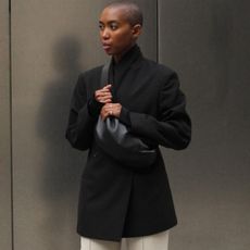 Woman wears black blazer, cream trousers and black handbag. 