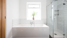 Clean white bathroom with plant on window sill, a wide deep bath, and walk in shower with glass doors, silver fittings and white subway tiling on walls
