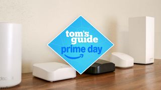 Several mesh routers lined up on a shelf with the Tom's Guide Prime Day deals badge in the middle