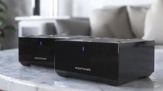 Netgear Nighthawk MK62 double pack displayed on a marble coffee table in a living room.