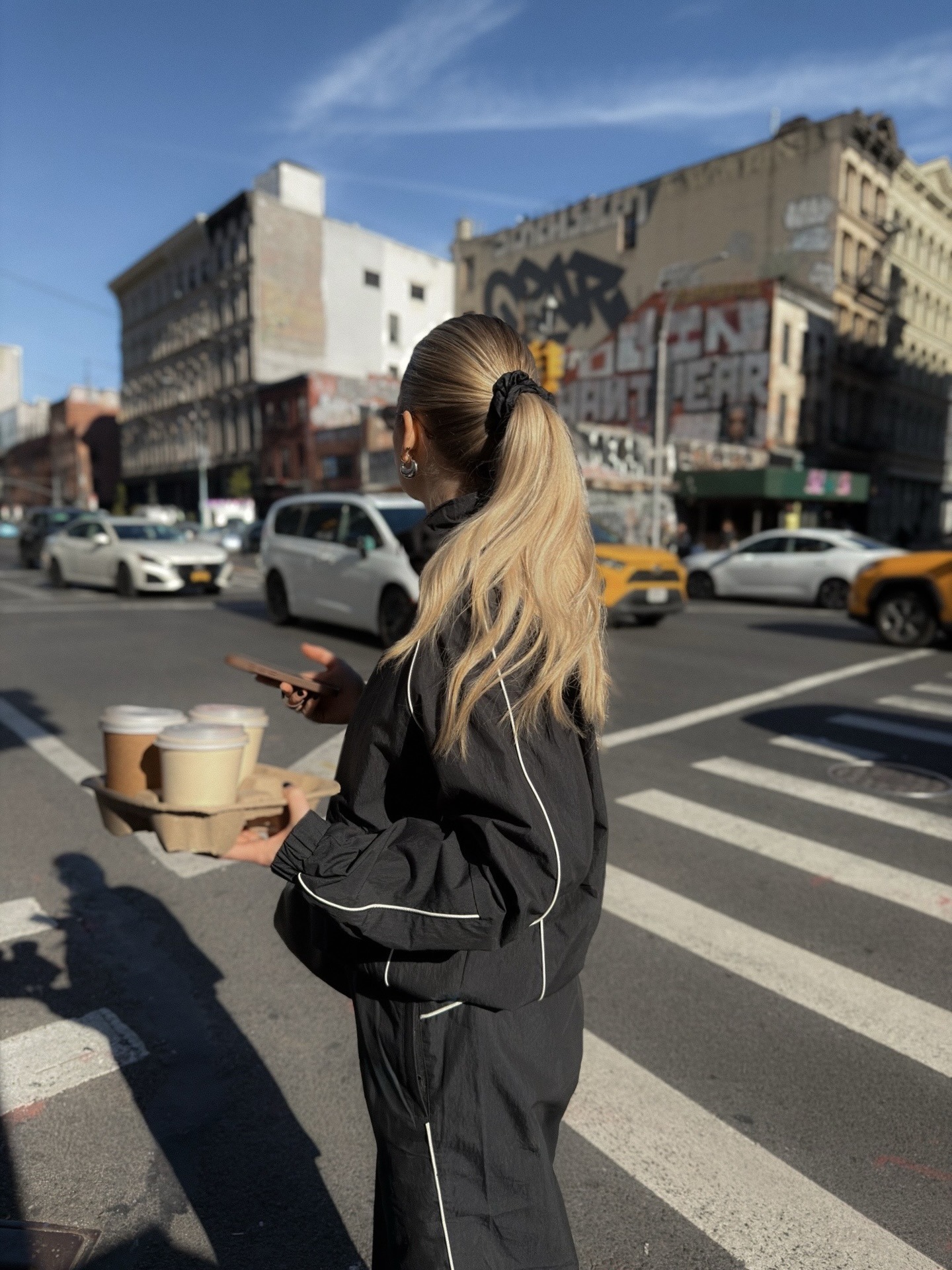 A woman holding takeaway coffees with a long, wavy ponytail