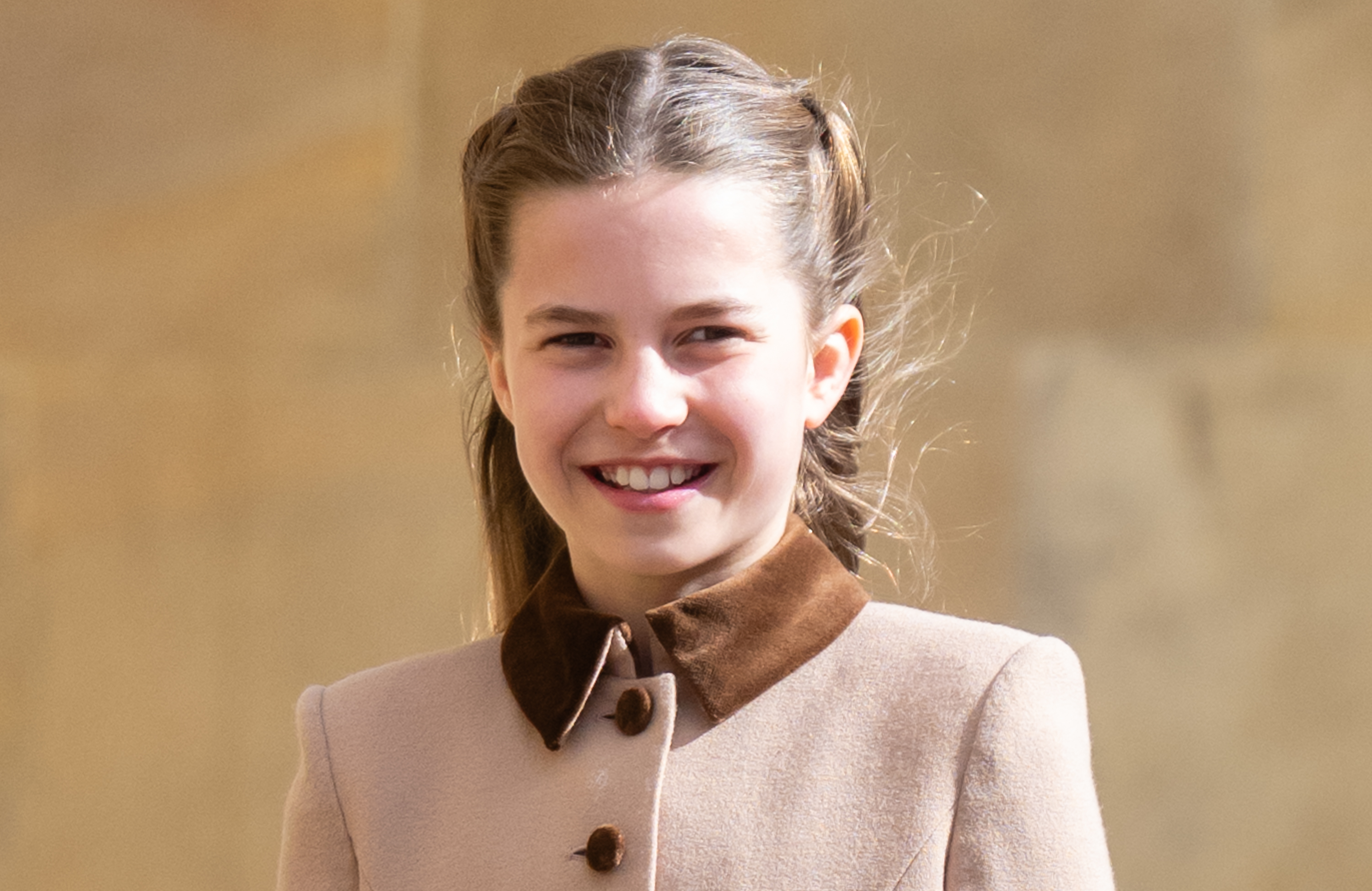 Princess Charlotte smiling in a tan coat