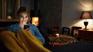 Woman sitting on couch with phone, face illuminated in the evening light